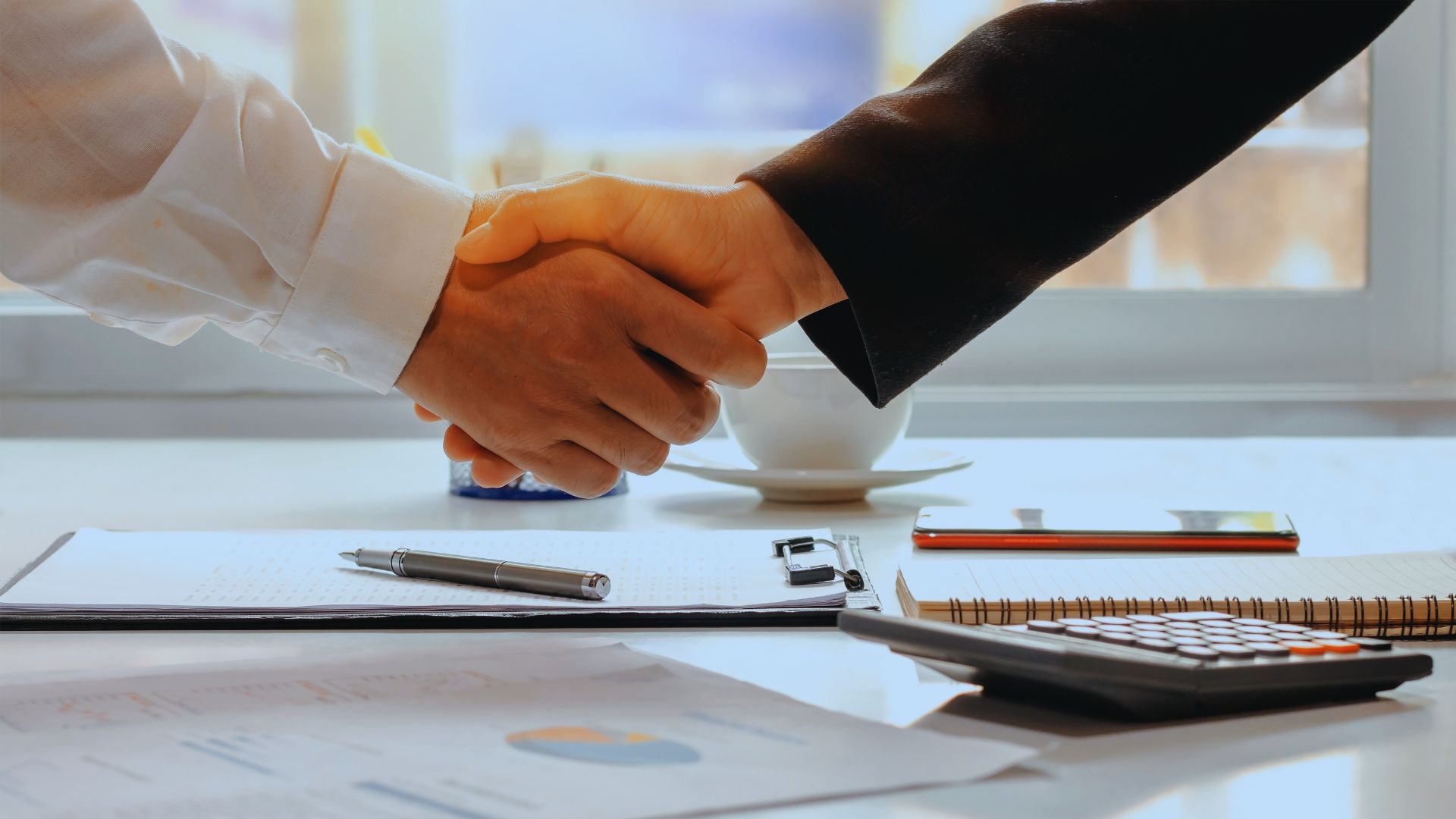 Handdruk tussen twee professionals aan een bureau, symbool voor samenwerking en HR als strategische partner.